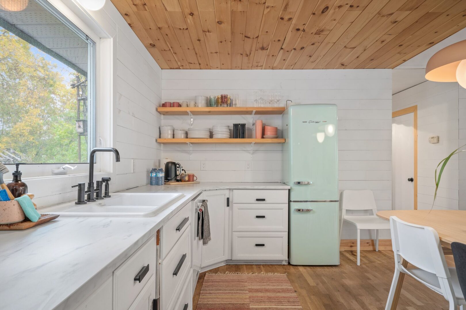 A modern kitchen with white cupboards and retro-looking appliances. The fridge is tall and skinny, and is a seafoam green colour.