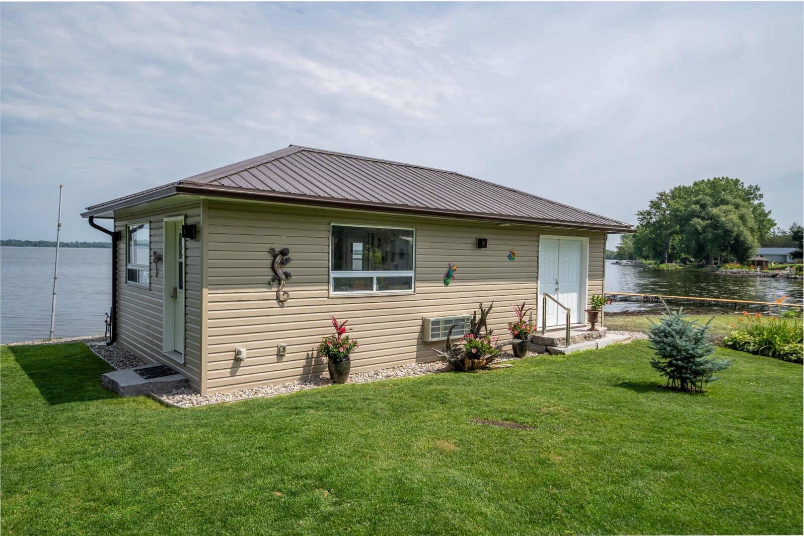 A big, four-season bunkie sits on a grassy lot by the water.