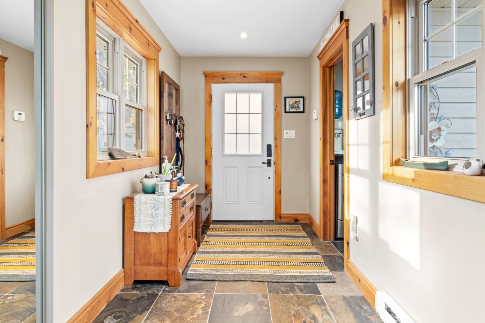Inside the front entrance of a luxury cottage, with tile flooring, lots of natural light, and light-coloured wood trimming the door and window frames.