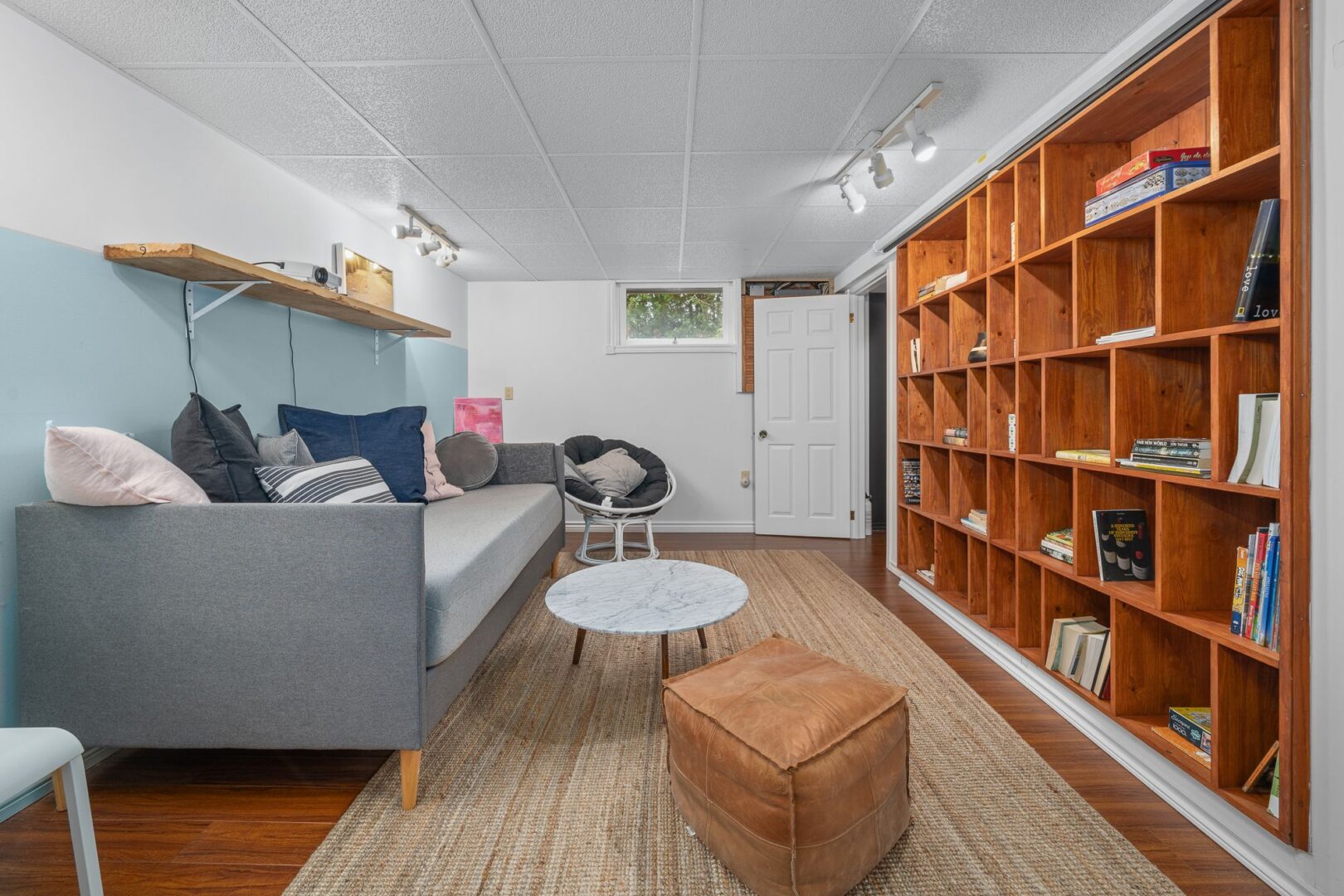 A finished basement area with lots of seating, light blue walls, and a wall of floor-to-ceiling wooden shelves.