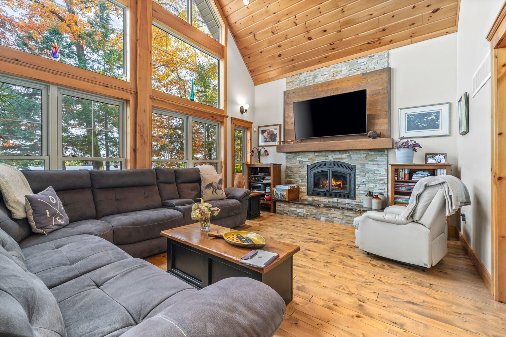 A bright living area with hardwood floors, floor-to-ceiling windows, a big sectional couch, and a television.
