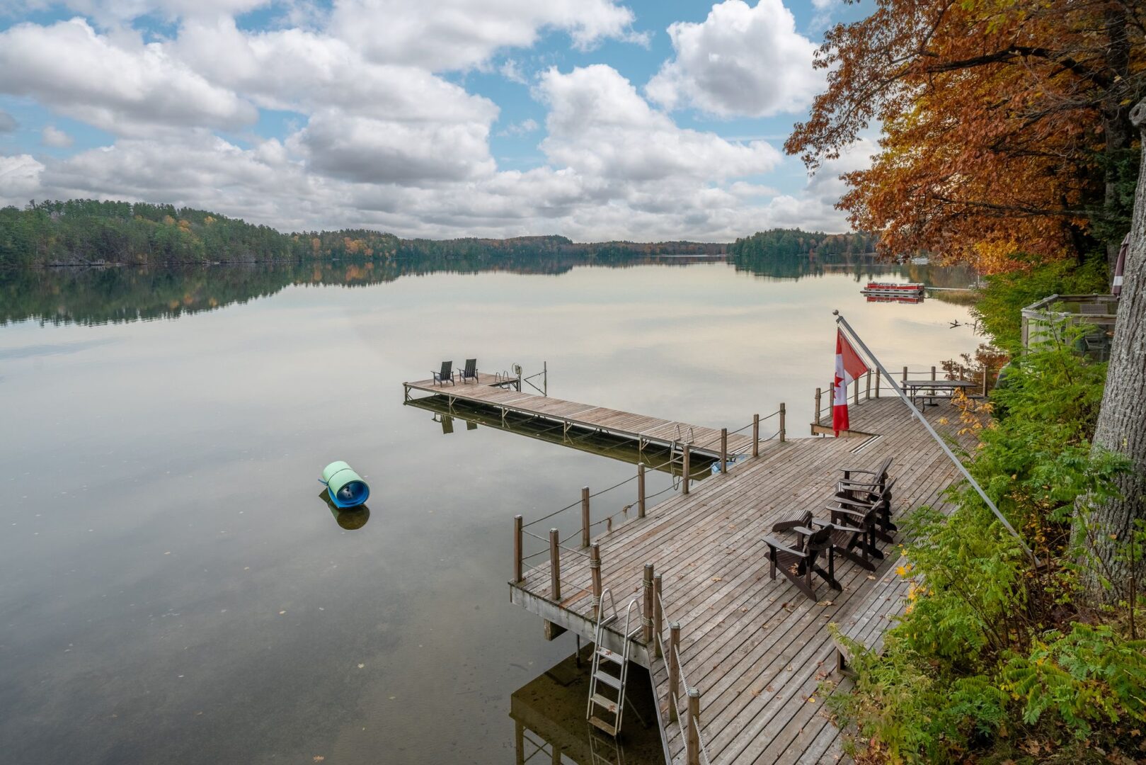 A large, wide dock spans the shoreline of a cottage property. A long, narrow piece of dock extends out into the lake.