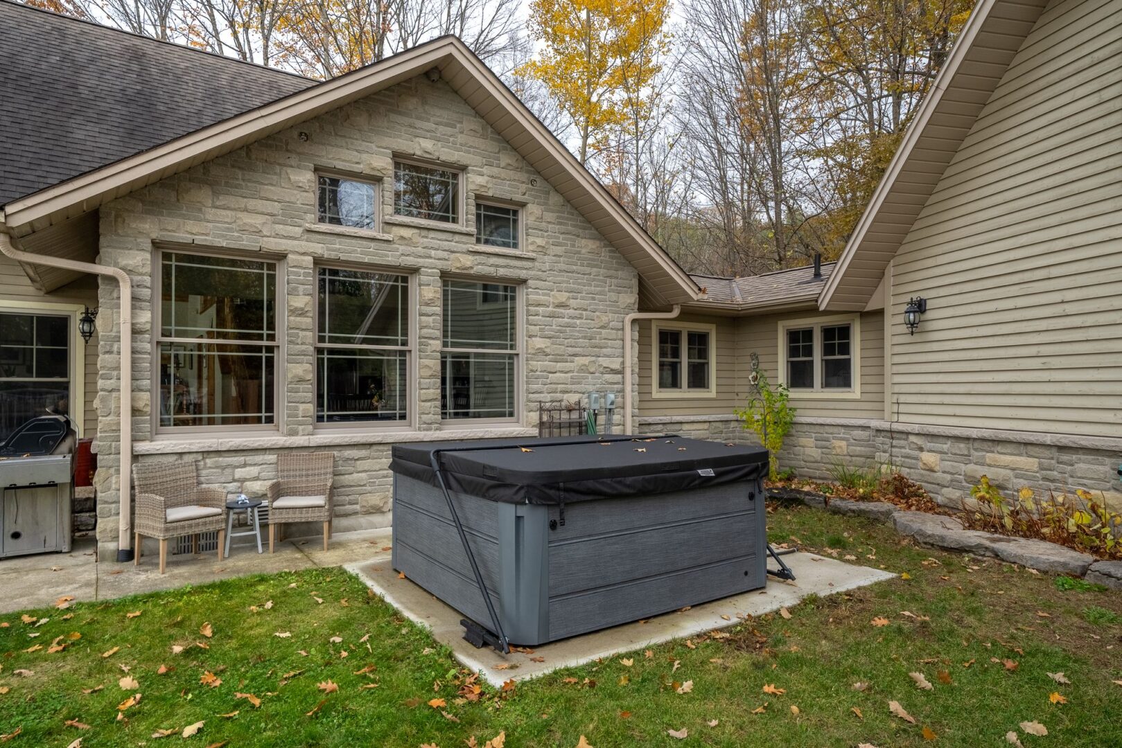 A hot tub sits on a small patio in front of a luxurious cottage.