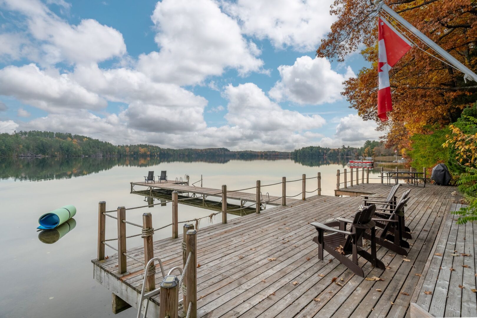 A large, wide dock spans the shoreline of a cottage property. A long, narrow piece of dock extends out into the lake.