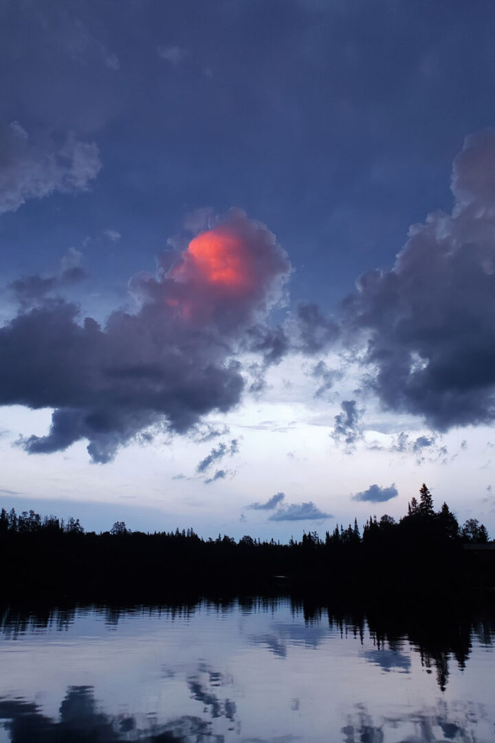Sunset on a lake after a rain storm, shadow of the trees on the water, red glow of the setting sun