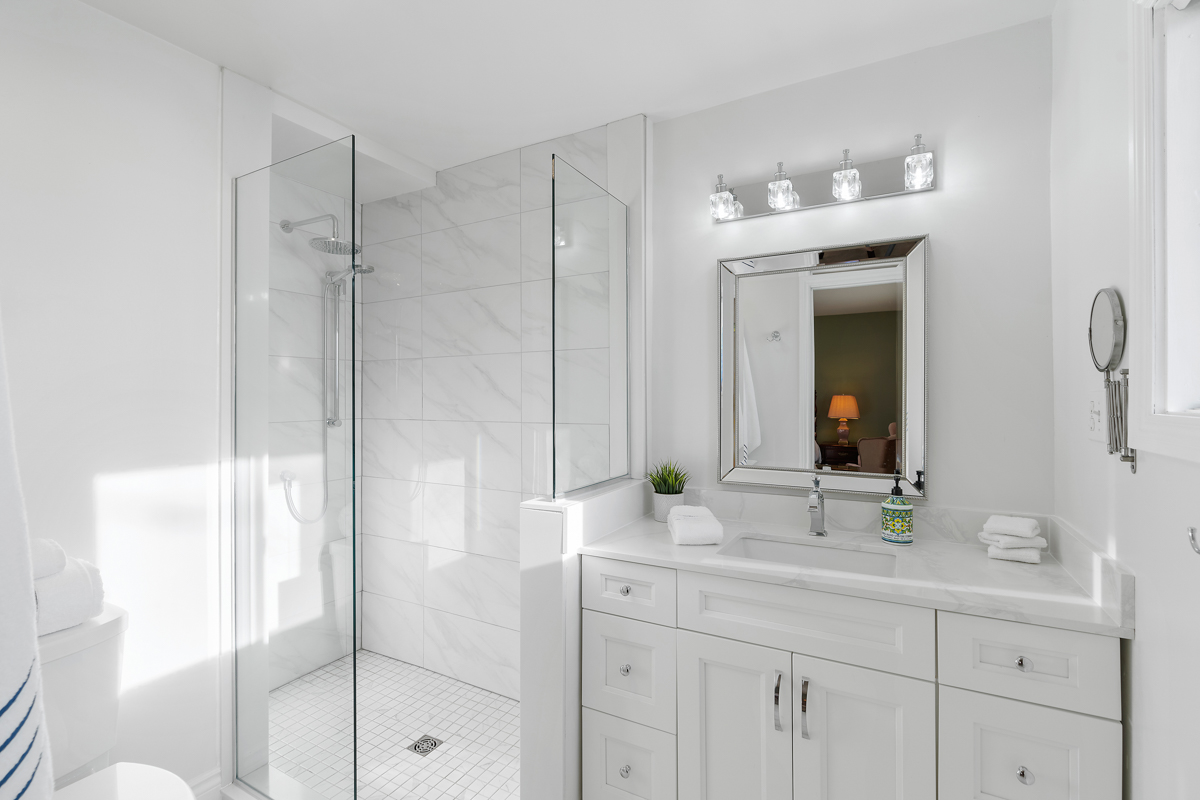 An all-white, updated three-piece bathroom with a walk-in shower, a toilet, and a sink.