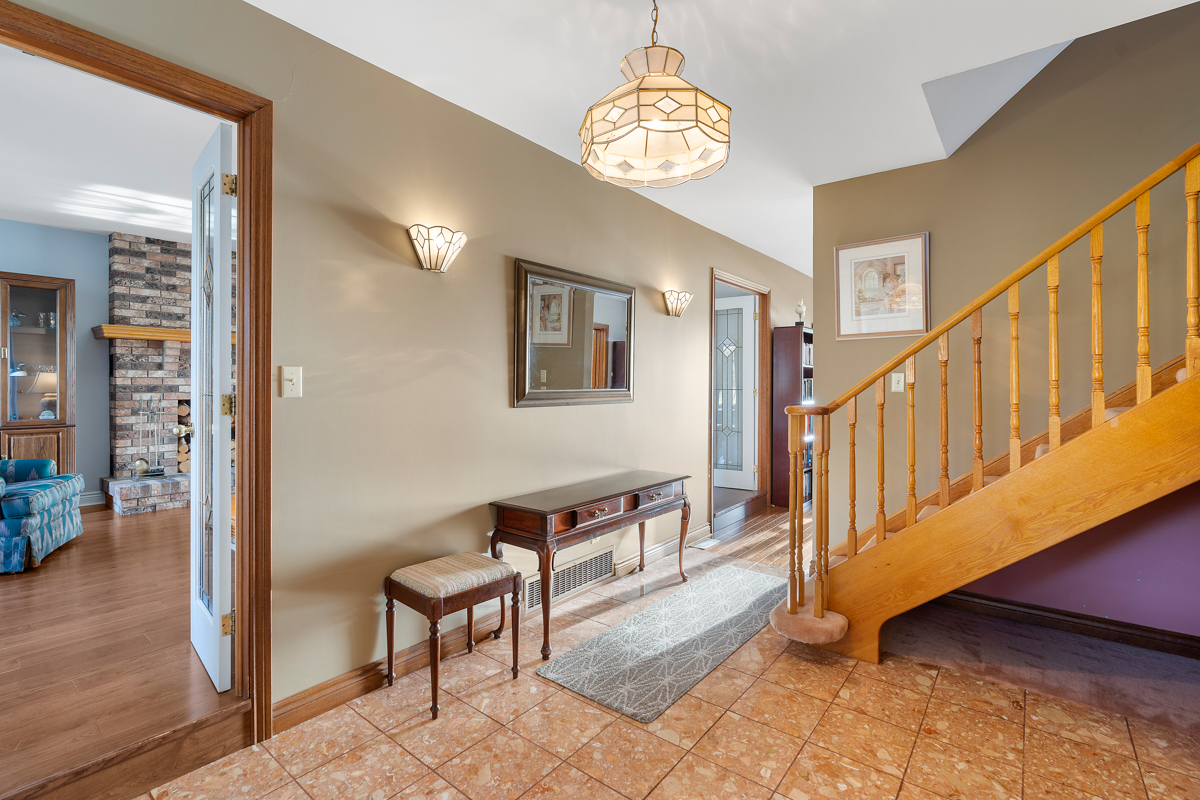 Inside the front foyer of a big home. The entrance area has tile floor. A bright hallway leads past a staircase to the second level.