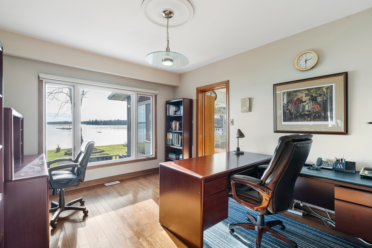 A bright office area with two big desks, hardwood floors, and a large window with a lake view.