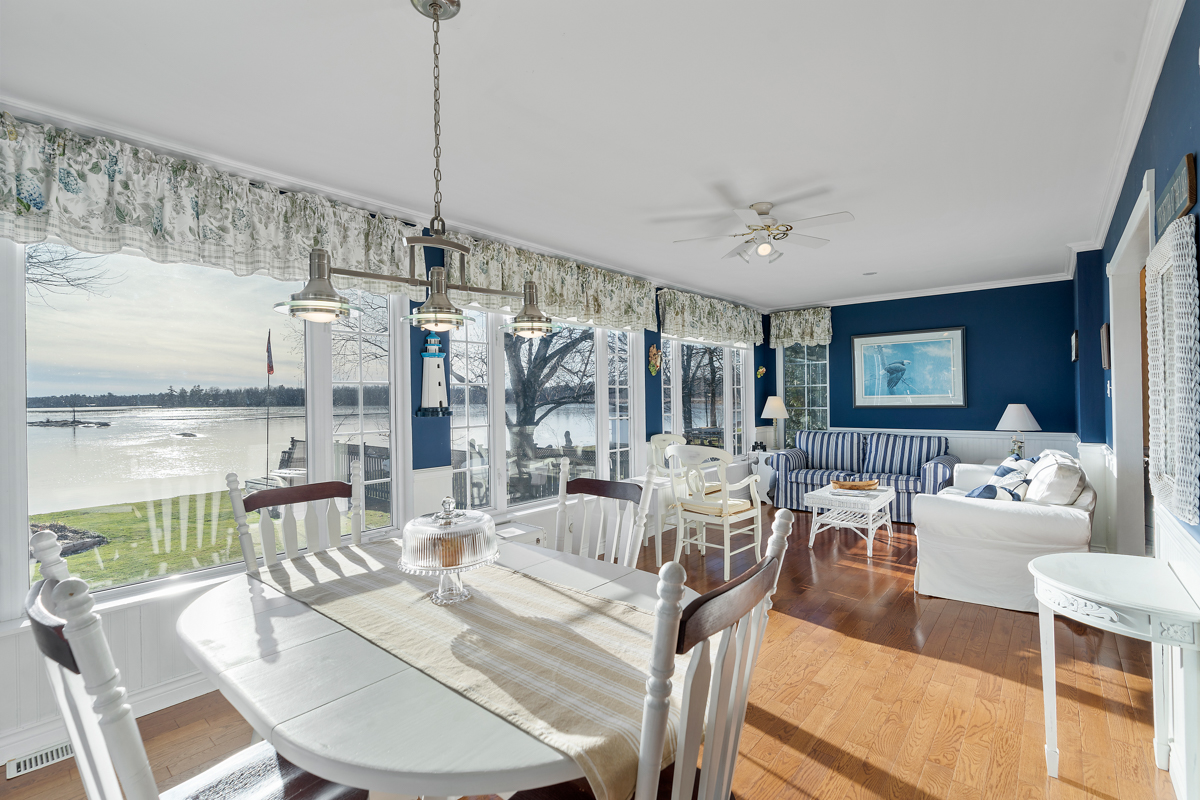 A bright, open-concept dining area that flows into a sunny sitting area, with plenty of windows, navy blue accents, and white furniture.