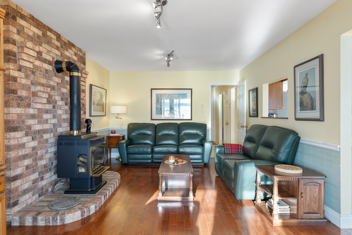 A cozy living area with cushy, dark green couches and hardwood floors. A wood stove sits on one side of the room, on floor-to-ceiling stone.