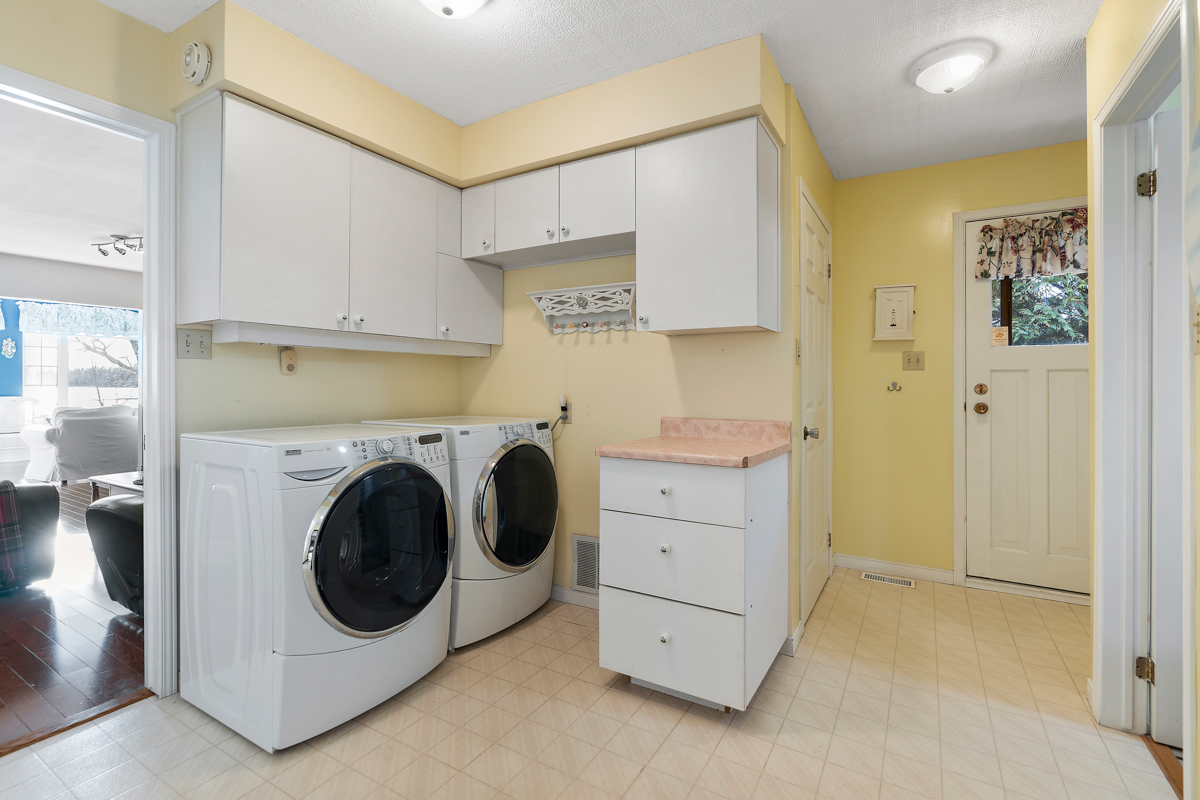 A spacious laundry room with a washing machine, a dryer, white cupboards, and yellow walls.