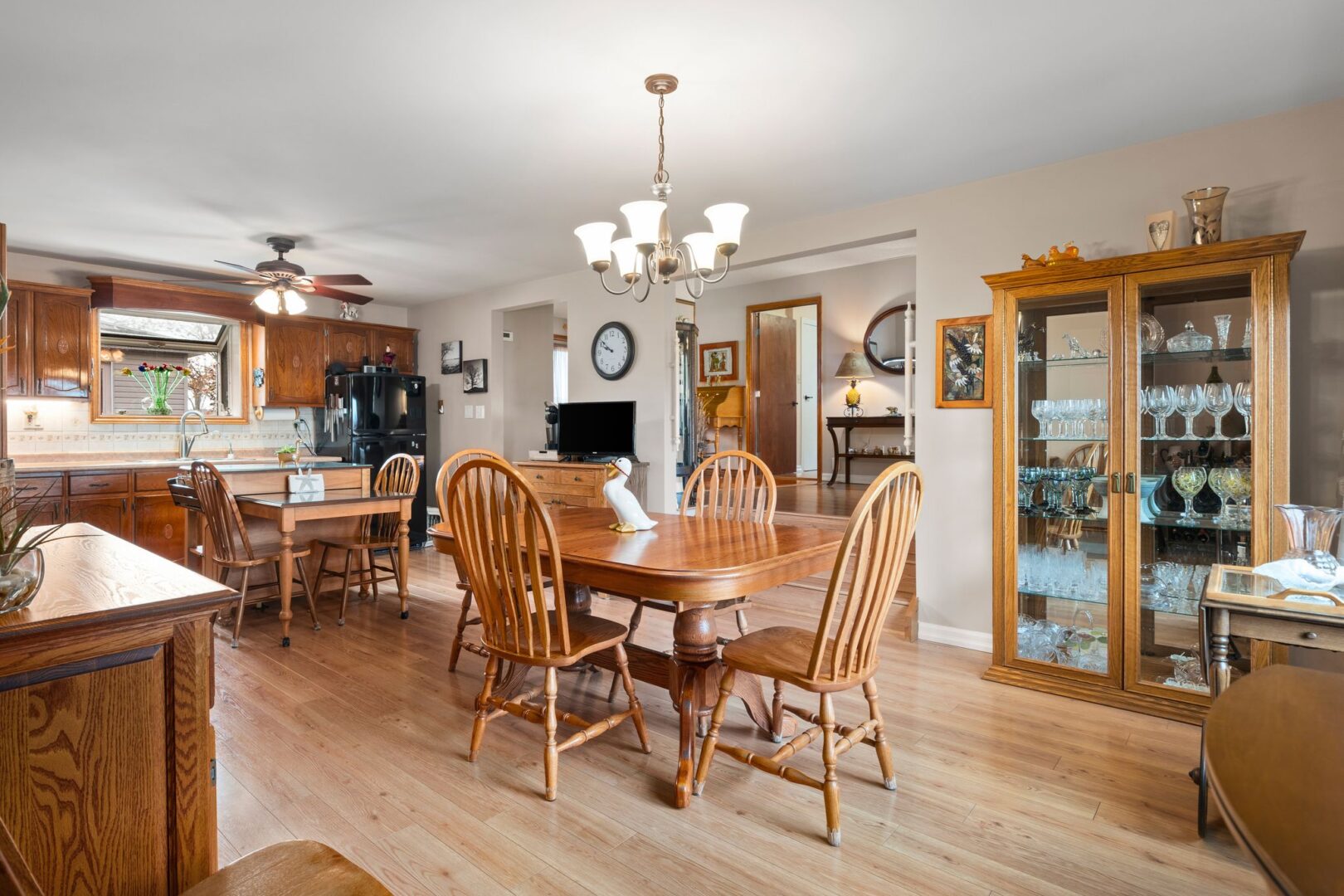 A bright dining area with hardwood flooring; a table and chairs; and a cabinet with glass doors and dishes inside.