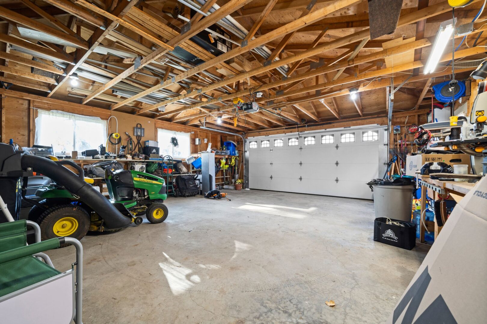 Interior of a garage with a concrete floor and mostly open space. A John Deere ride-on mower sits in the garage.