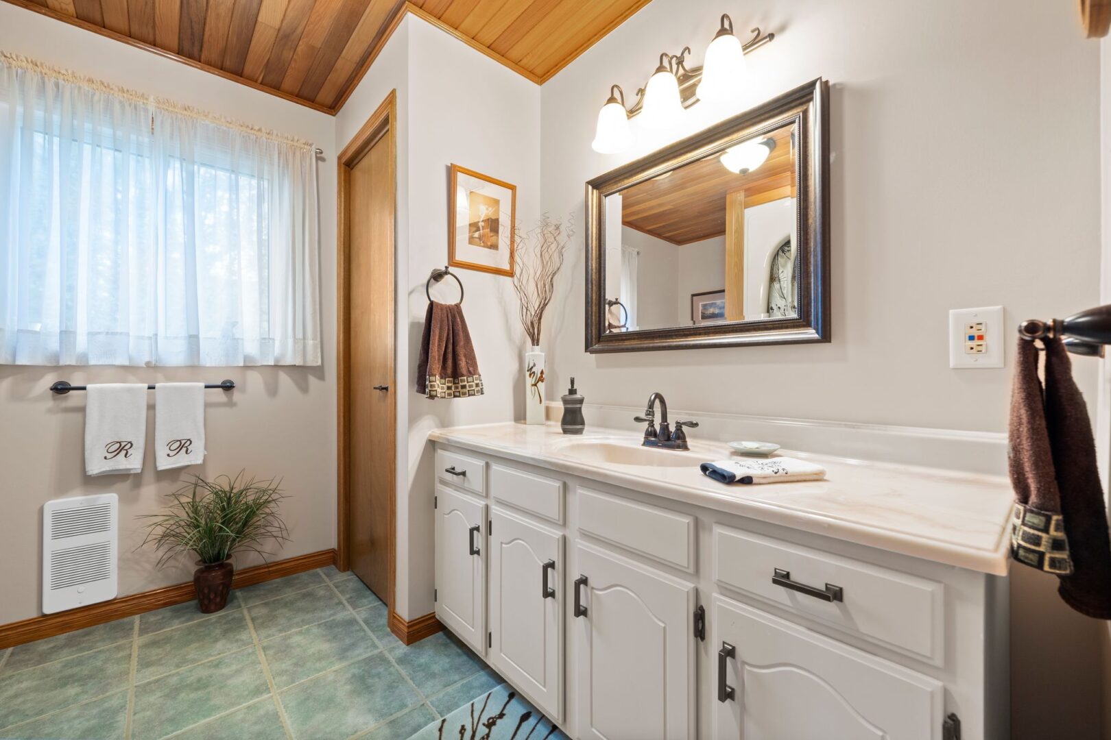 A big bathroom with green tile flooring and white cupboards under the sink.
