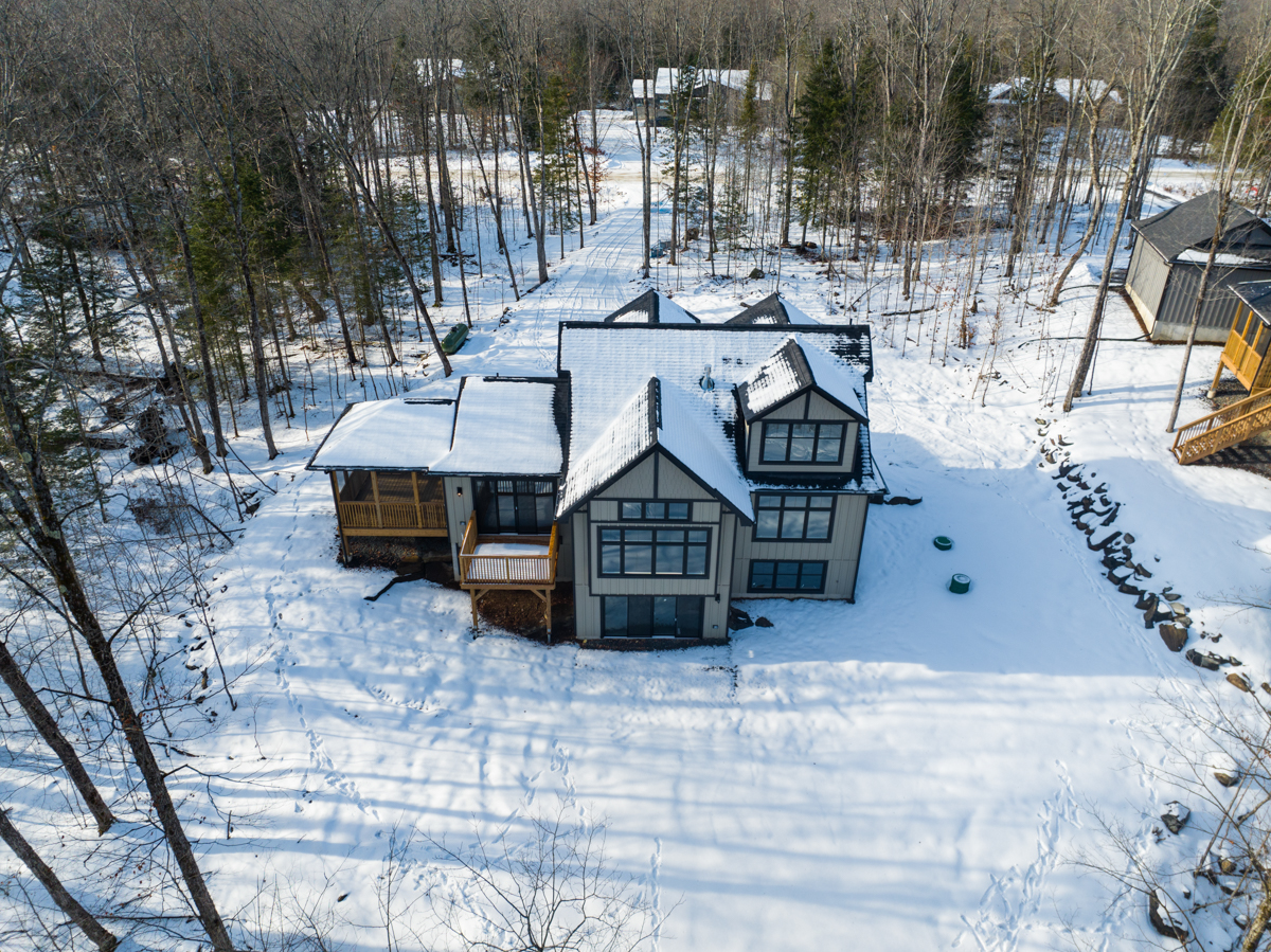 A large home sits in a clearing of a wooded, rural area. There is snow on the ground and the trees are bare.