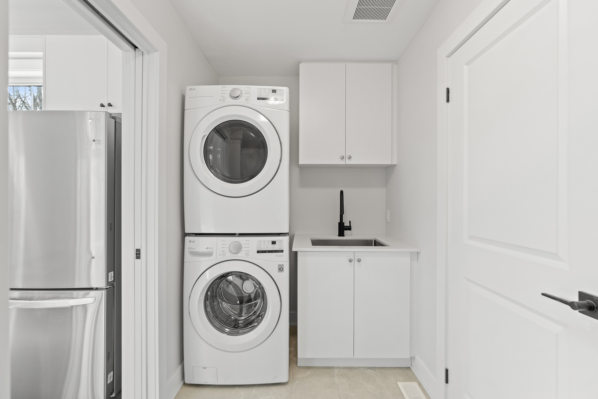 A small room with a stacked washing machine and dryer, a sink, and white cupboards.