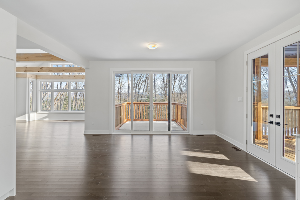 A bright area with dark hardwood floors, white walls and a white ceiling. Sliding glass doors open up into a sunroom ahead.