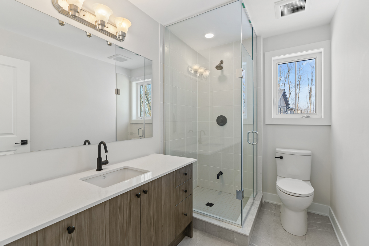 A big bathroom with a toilet, a sink, a walk-in shower, and a window.