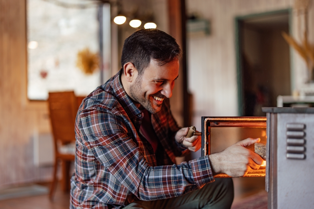 A man placing a small log into a woodstove