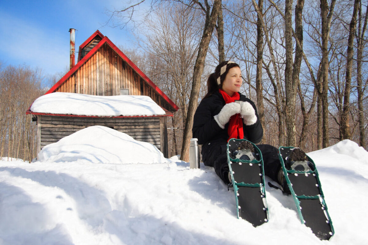 a woman sitting in front of a cabin wearing snowshoes