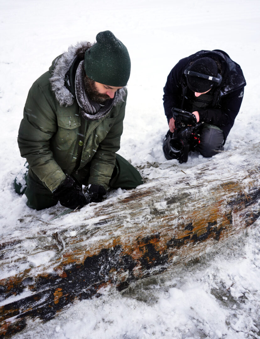 Two men in the water, inspecting a portion of a ship's wooden hull