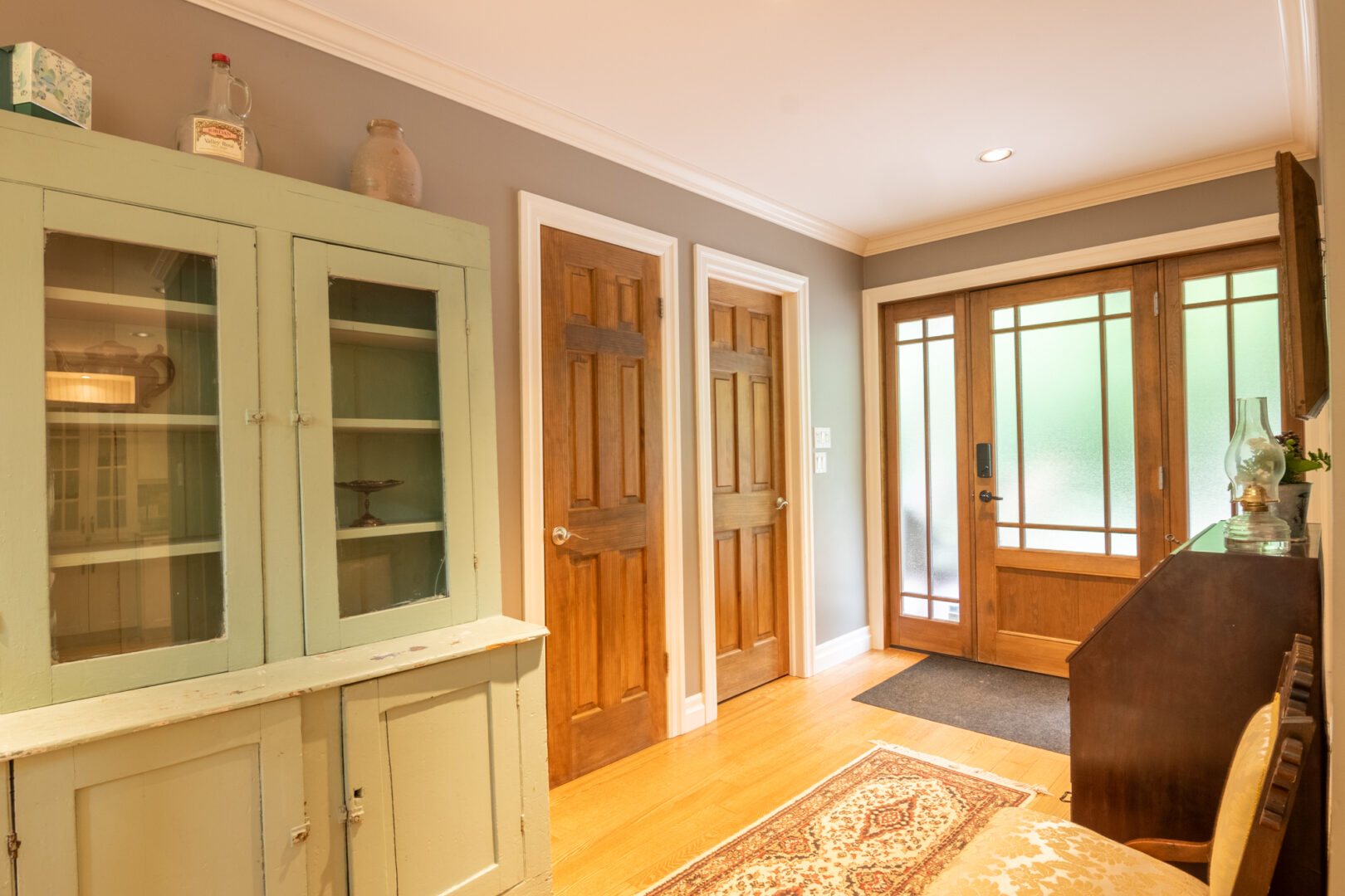 A bright entrance area with hardwood floors, wood doors, and antique-style furniture.