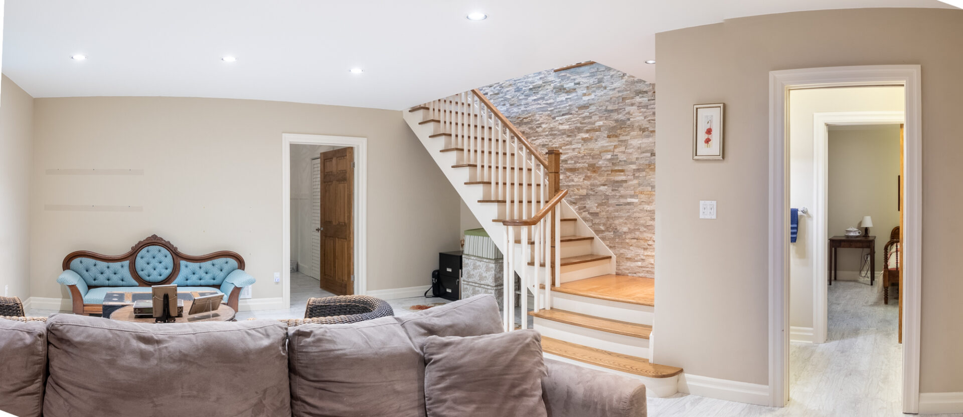 A small lower-level living space at the bottom of a staircase, with two couches. A doorway leads to a bathroom and a bedroom.