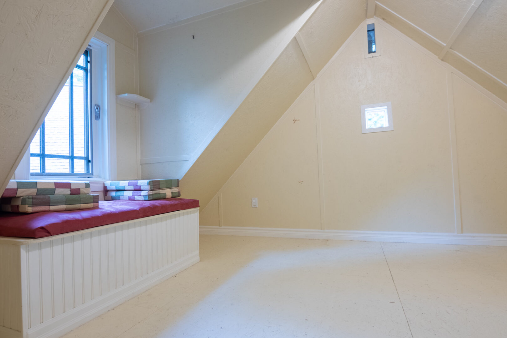 A small loft space with white walls, a peaked ceiling, and a window seat.