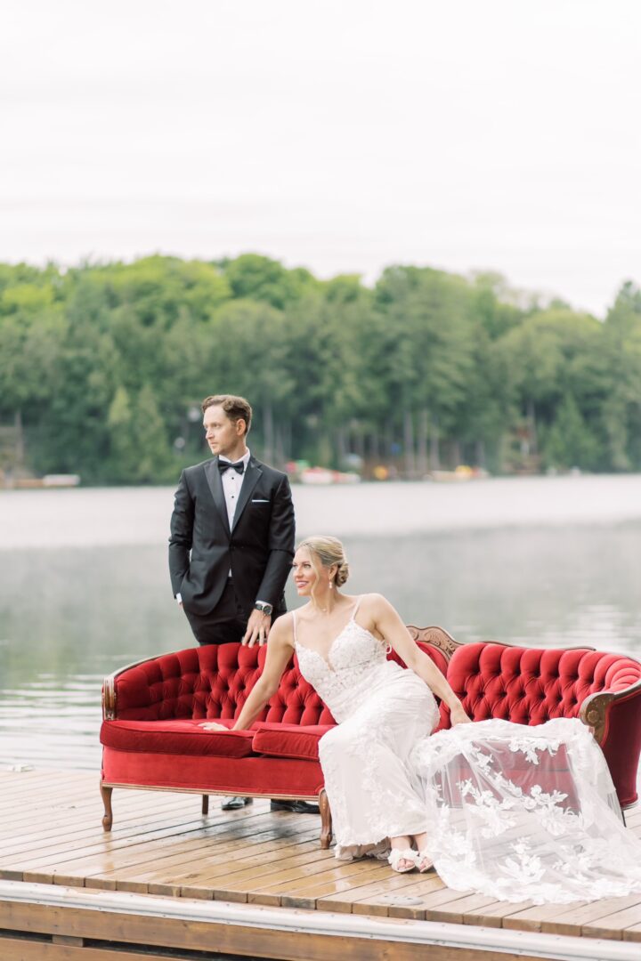 natalie spooner in a wedding dress and her husband in a suit sitting on a red couch on the dock