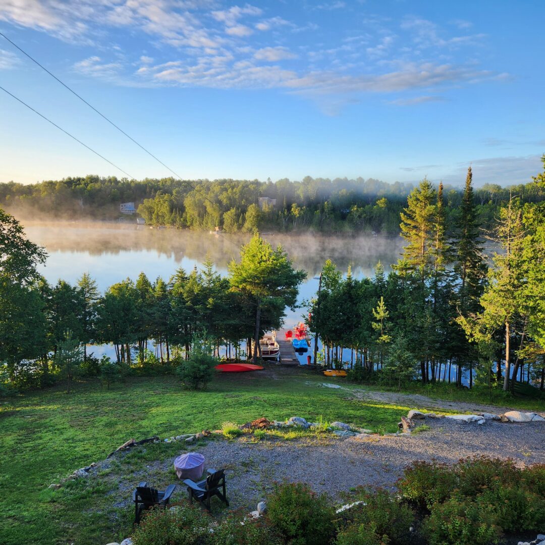 View across a manicured, grassy lot, looking out toward a tree-lined shore of a lake.