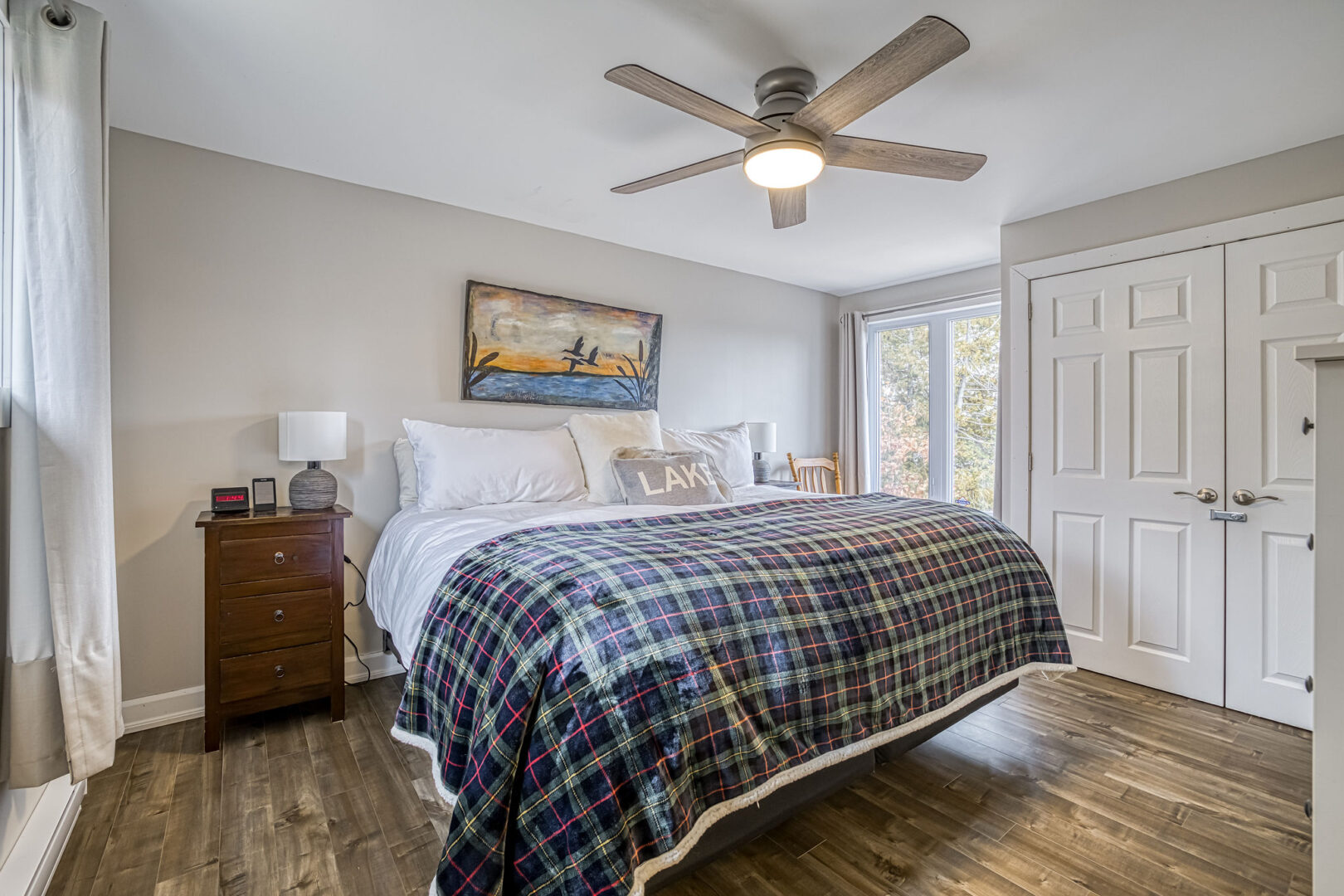 A large bedroom with a big bed, hardwood flooring, lots of windows, and double closet doors.