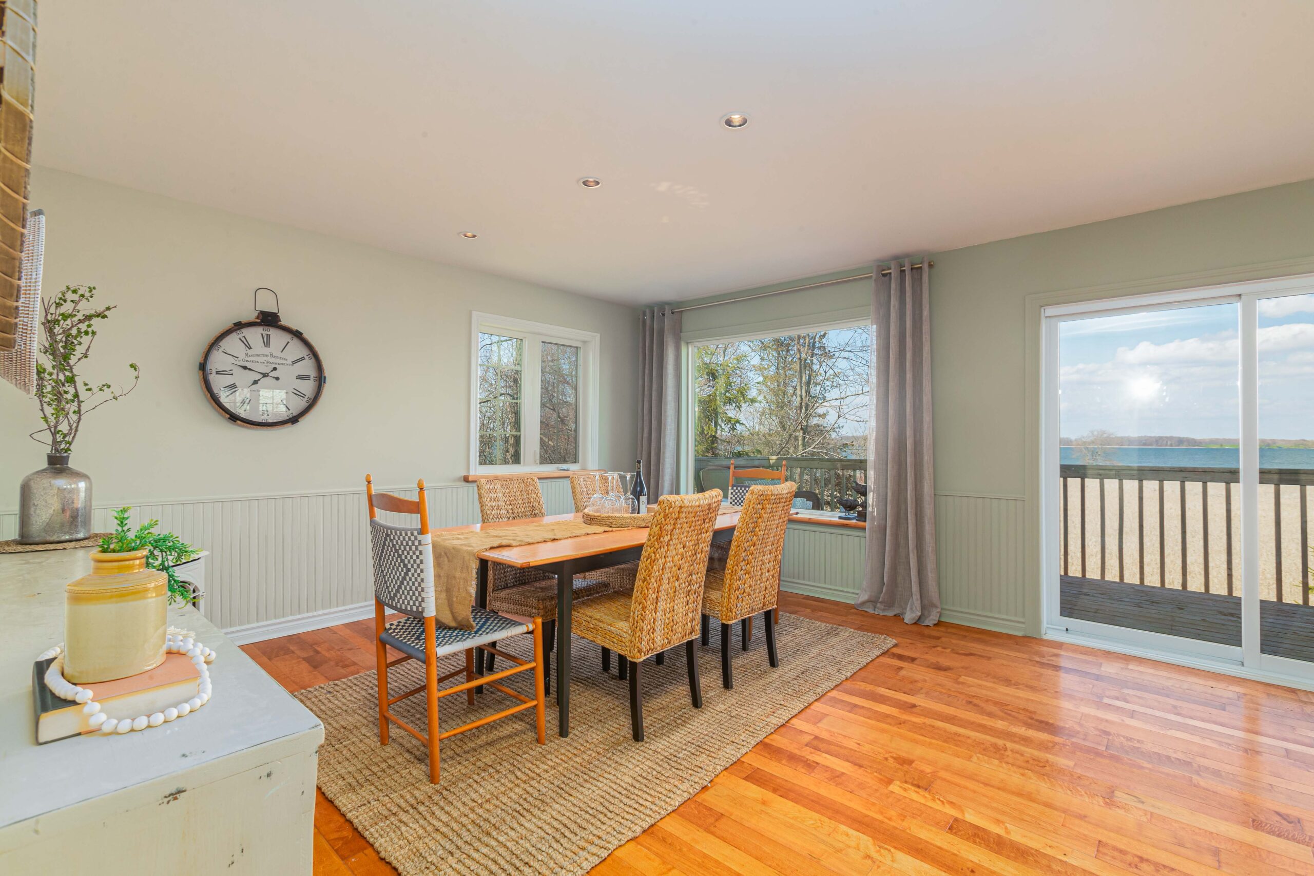 A bright dining area with a table and chairs, hardwood flooring, and big windows. Double glass doors open out to an exterior deck.