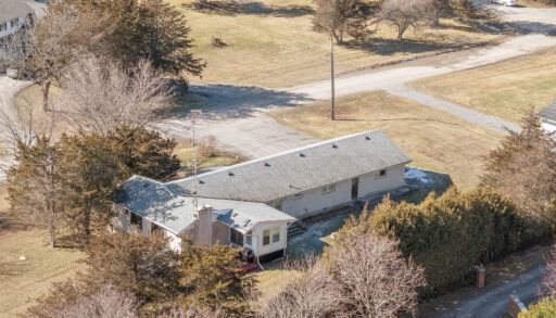 Overhead view of a bungalow sitting on a grassy area, surrounded by some trees.