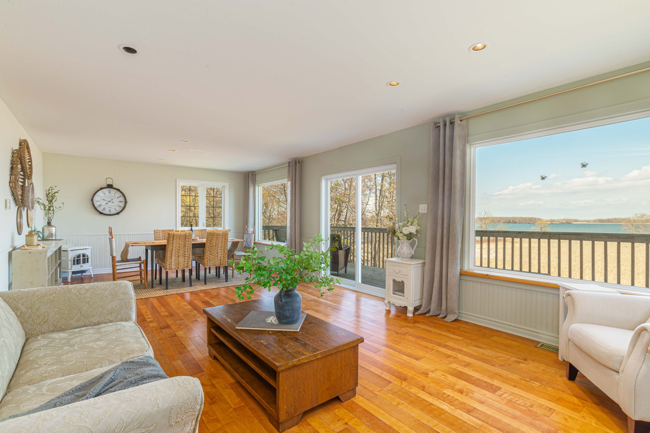 A bright living space with warm hardwood floors and lots of windows. There is a couch in the living area, and the far side of the room flows into a dining area with a table and chairs.