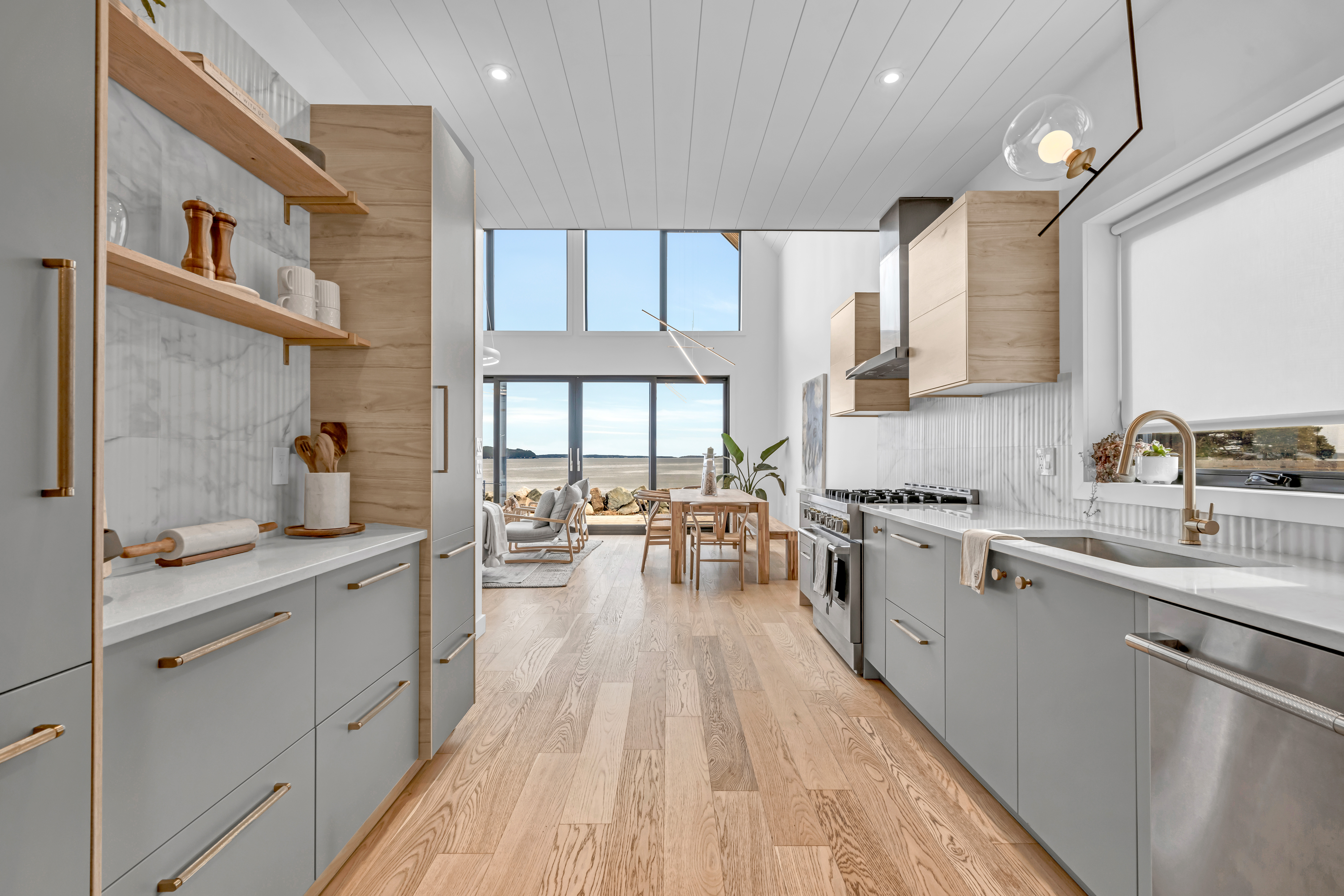 A big, bright, modern kitchen with light gray cabinetry, stainless steel appliances, light hardwood flooring, and lots of countertop space.