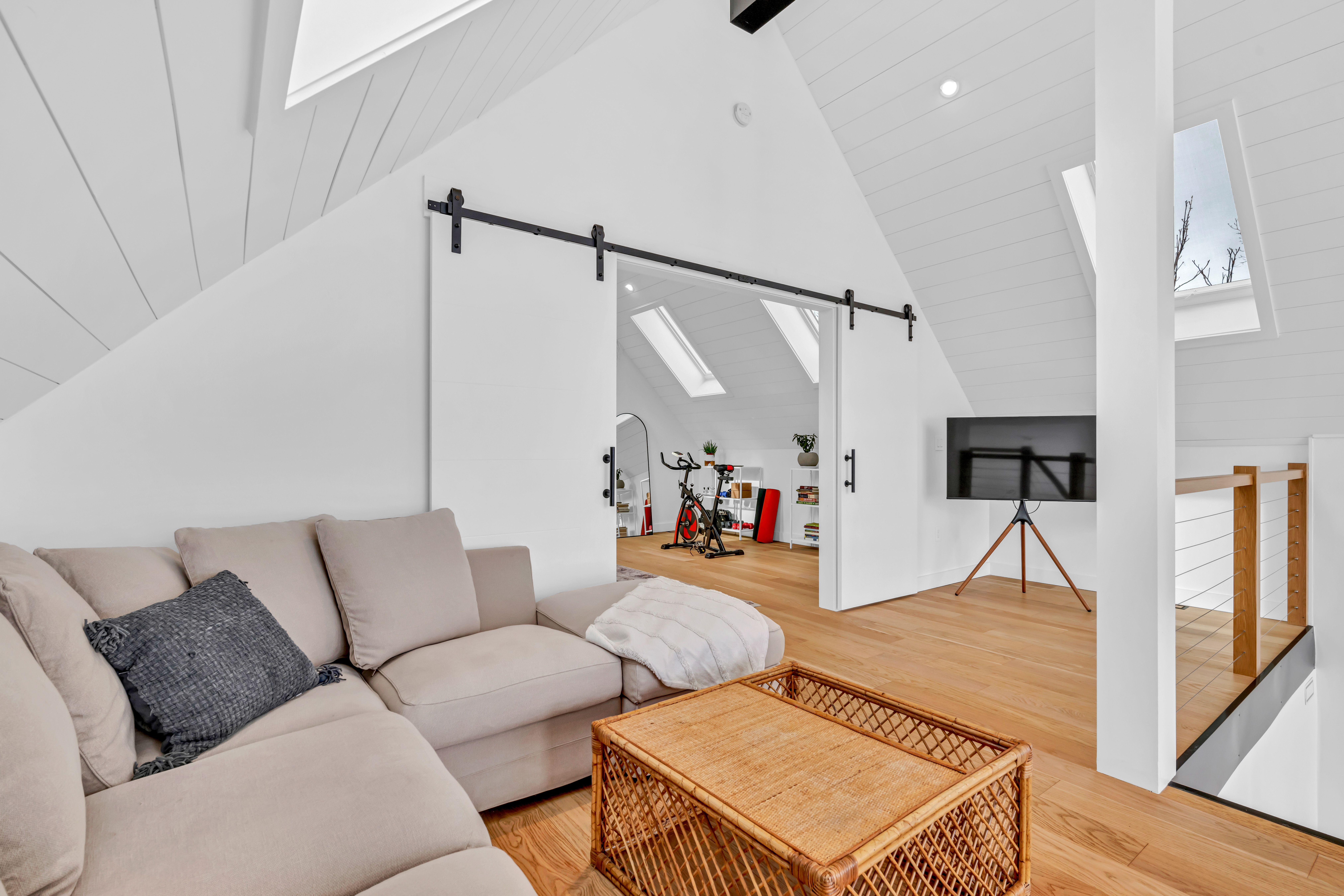 A small loft-level living space with a sectional couch and a television. Open sliding doors reveal a bedroom beyond the living area.
