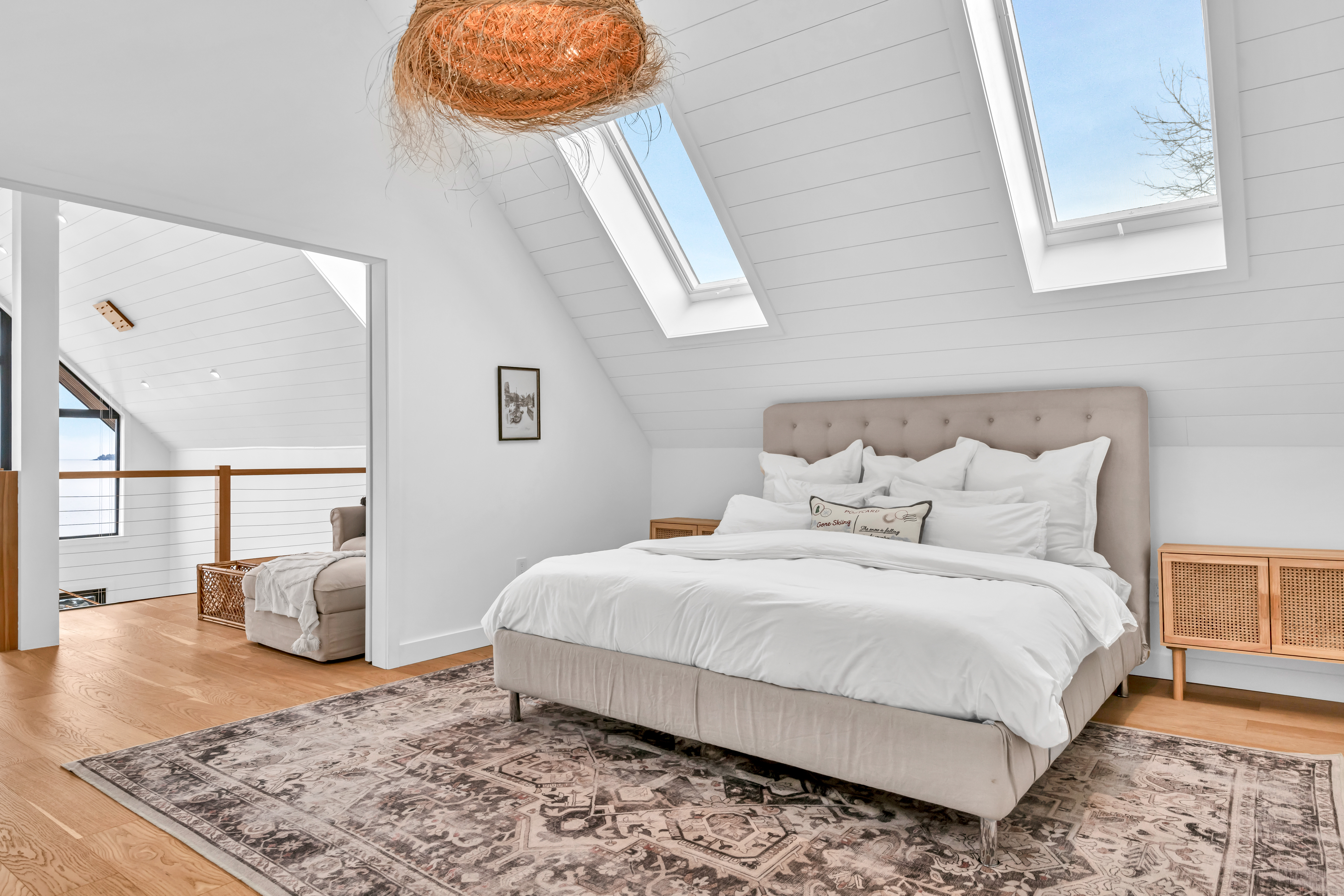A big bed in a bright, open room, on top of a large area rug on a hardwood floor. The slanted ceiling has two skylights, letting in lots of natural light.