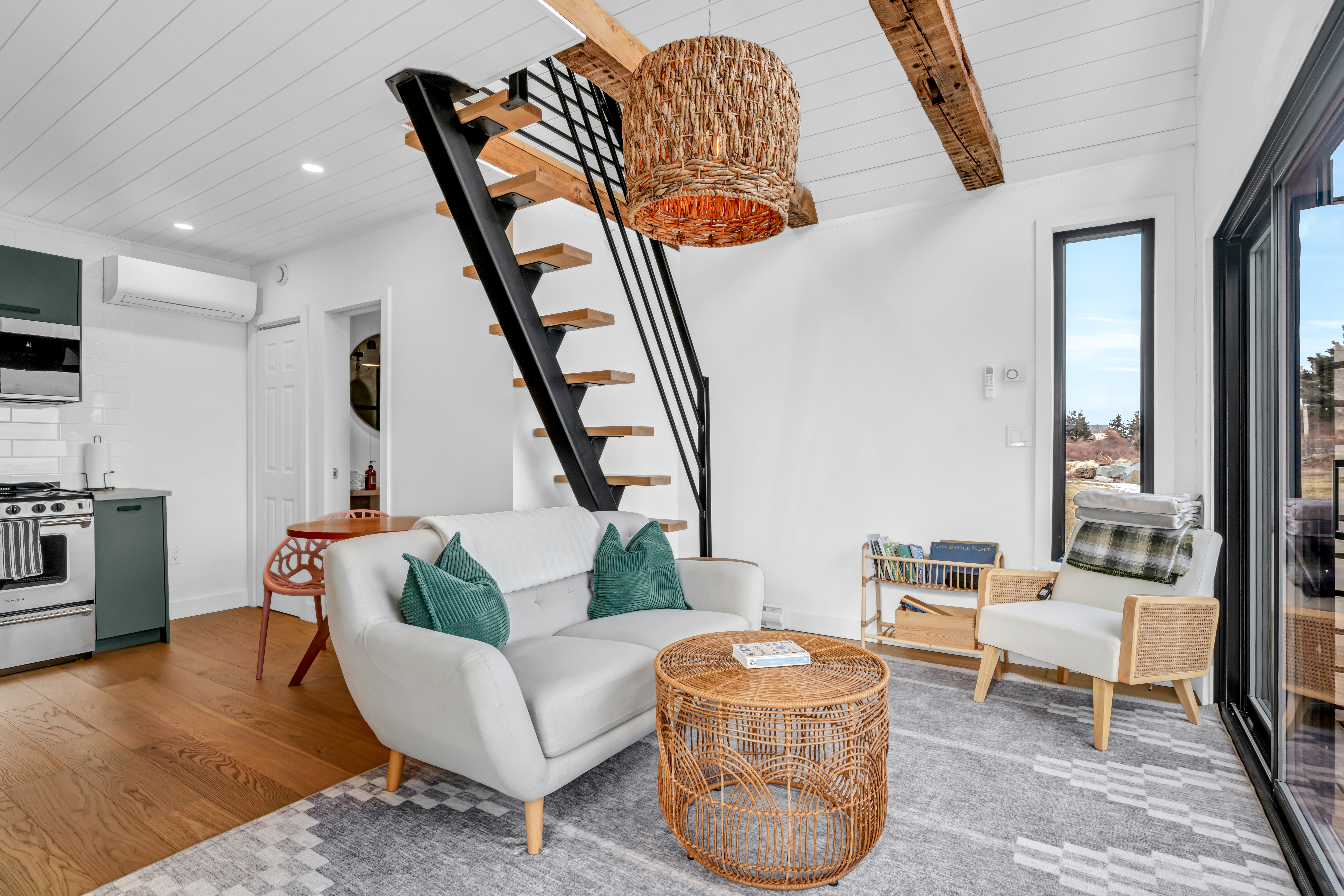 A small but bright living area with a couch and a chair. Stairs lead up to a second loft level.