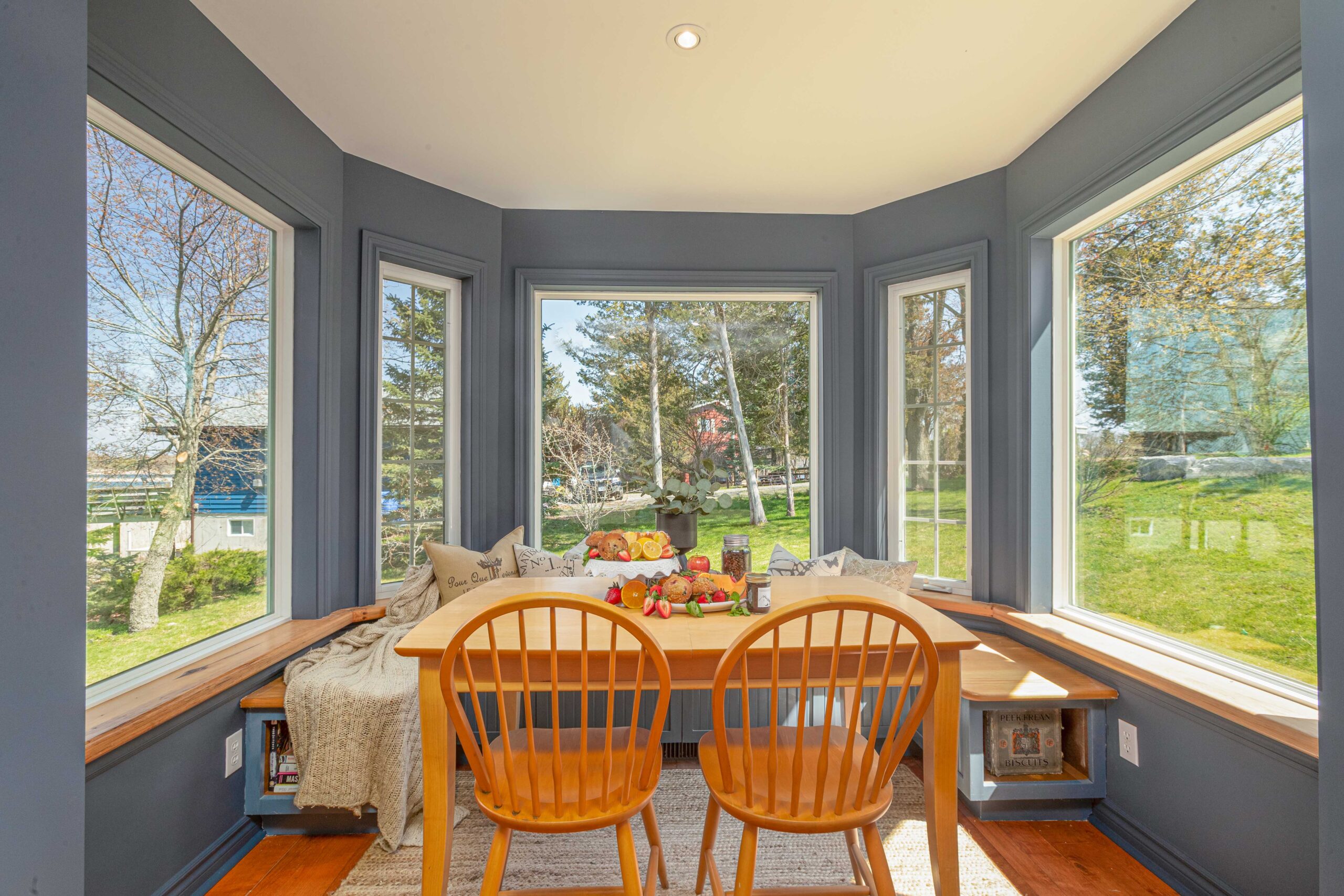 A small dining area in a round room with lots of windows. A window seat curves around the outer wall in front of the table, creating a little breakfast nook.