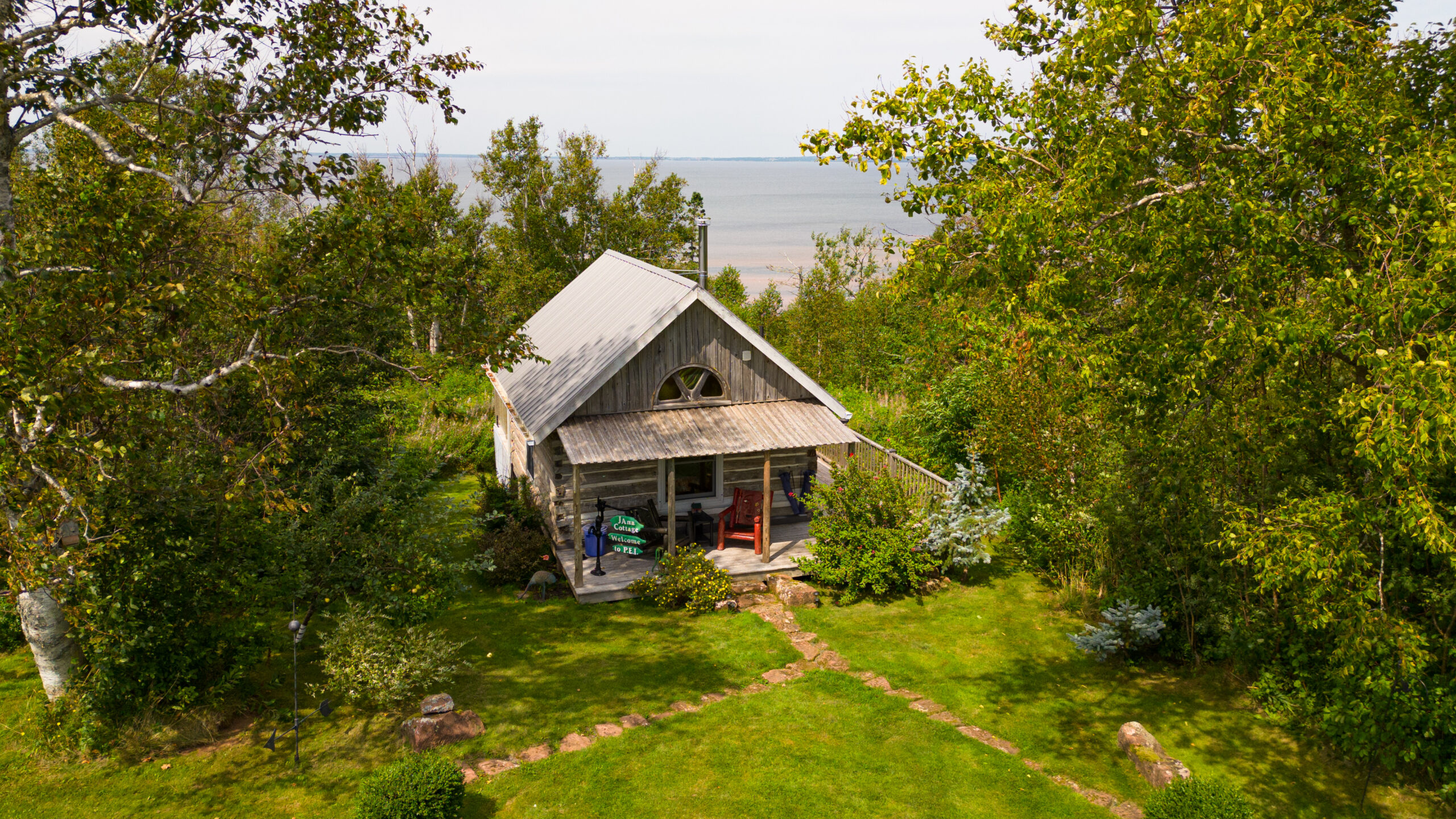 A small log cabin secluded by green trees, in front of the water.