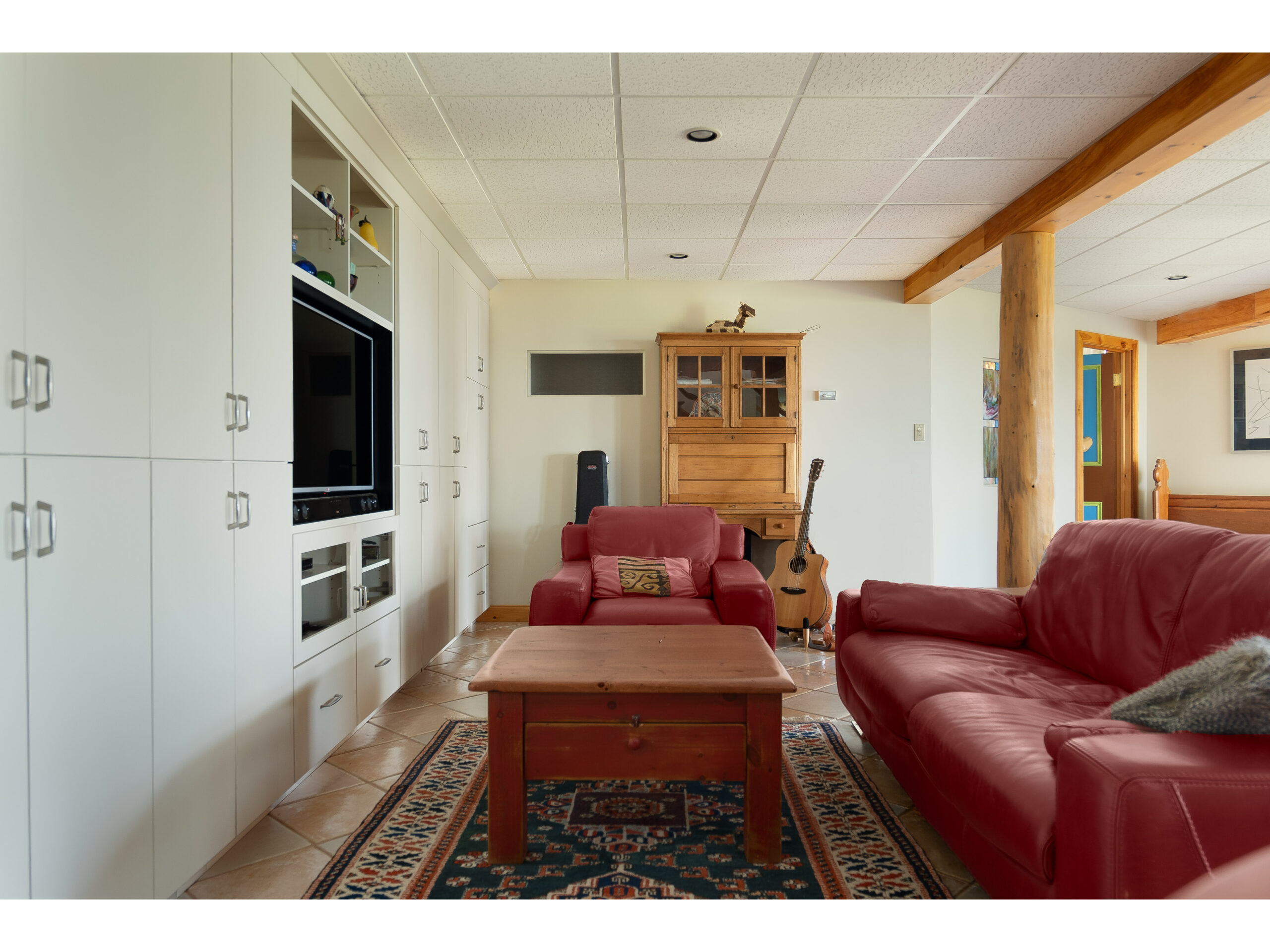 A red leather couch in a lower level living space. The couch faces a television, which is built into a wall of cupboards.