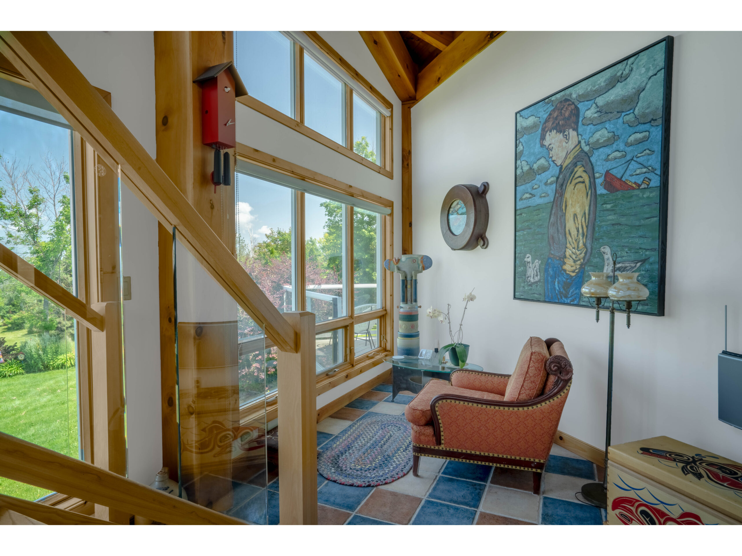 An arm chair facing the window at the bottom of a staircase. The flooring is made up of coloured tiles in red, blue, and beige.
