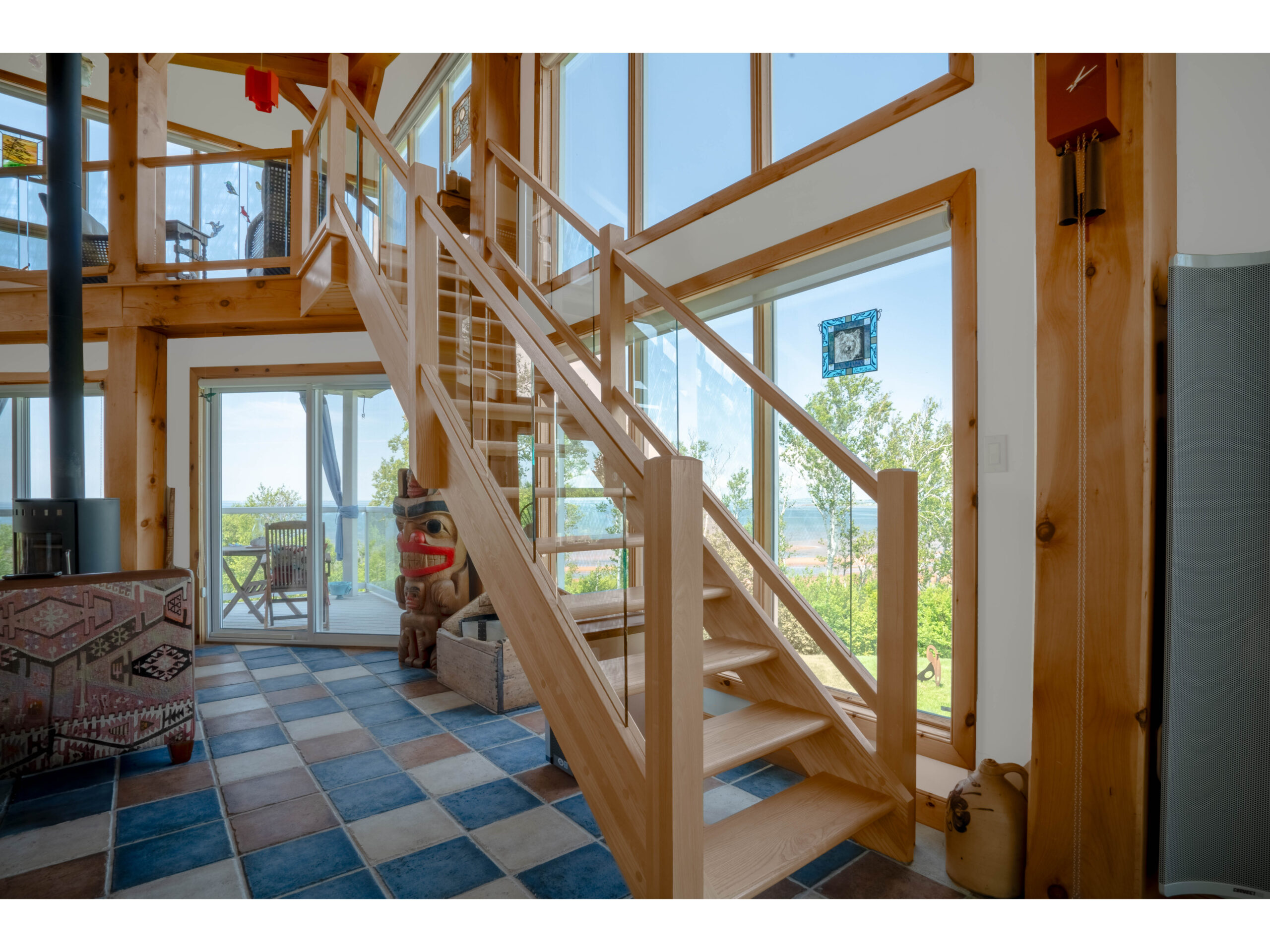 A wooden staircase leads up to a loft level in a big home with lots of windows.