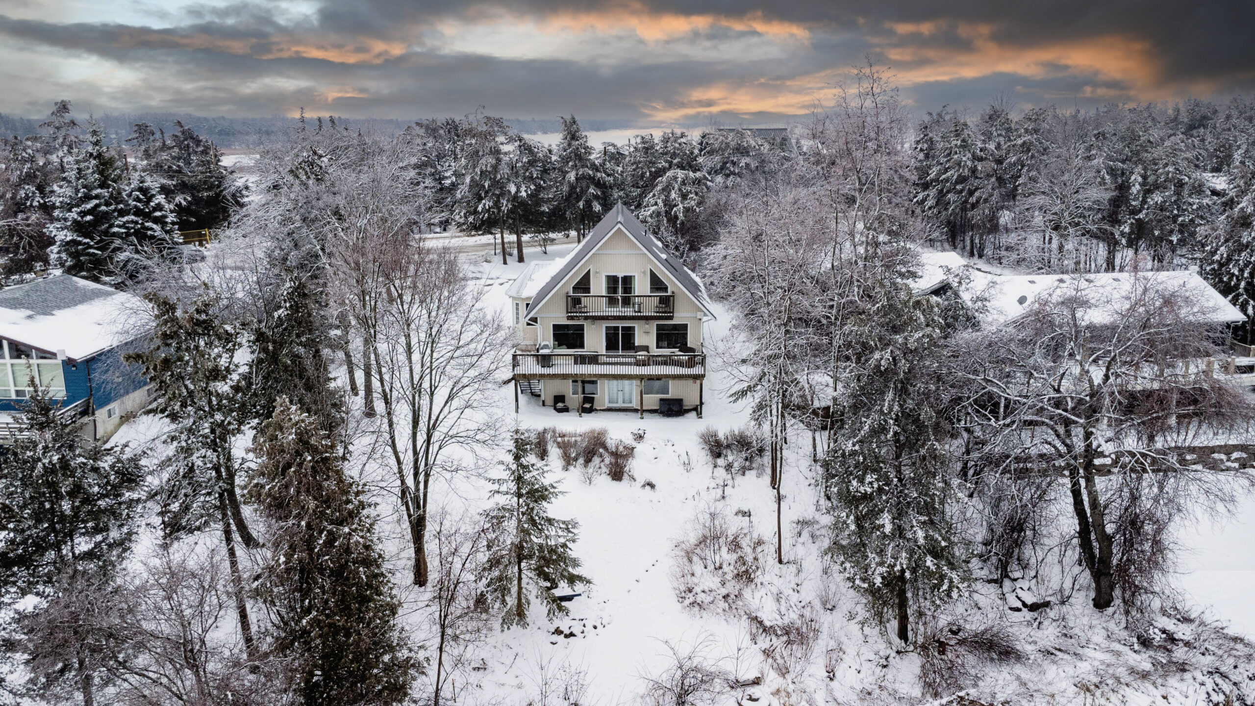 Overhead view of a large home on a snow-covered yard, surrounded by trees.