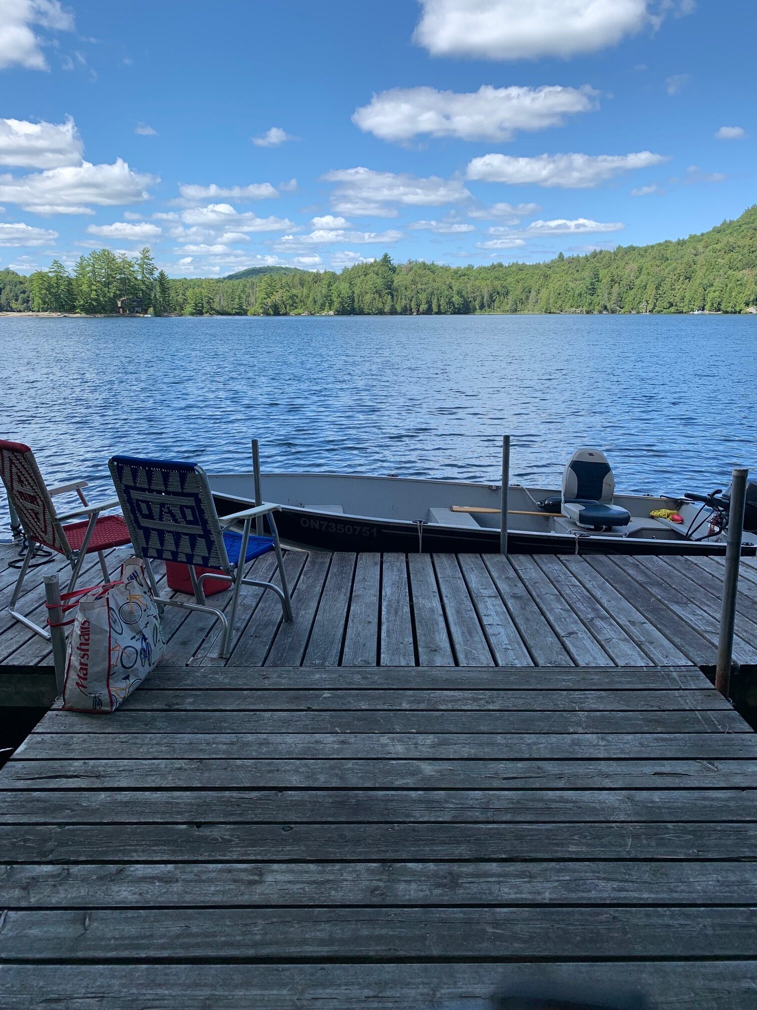 View from a wooden dock out over a blue lake. Green trees line the shore across the lake.