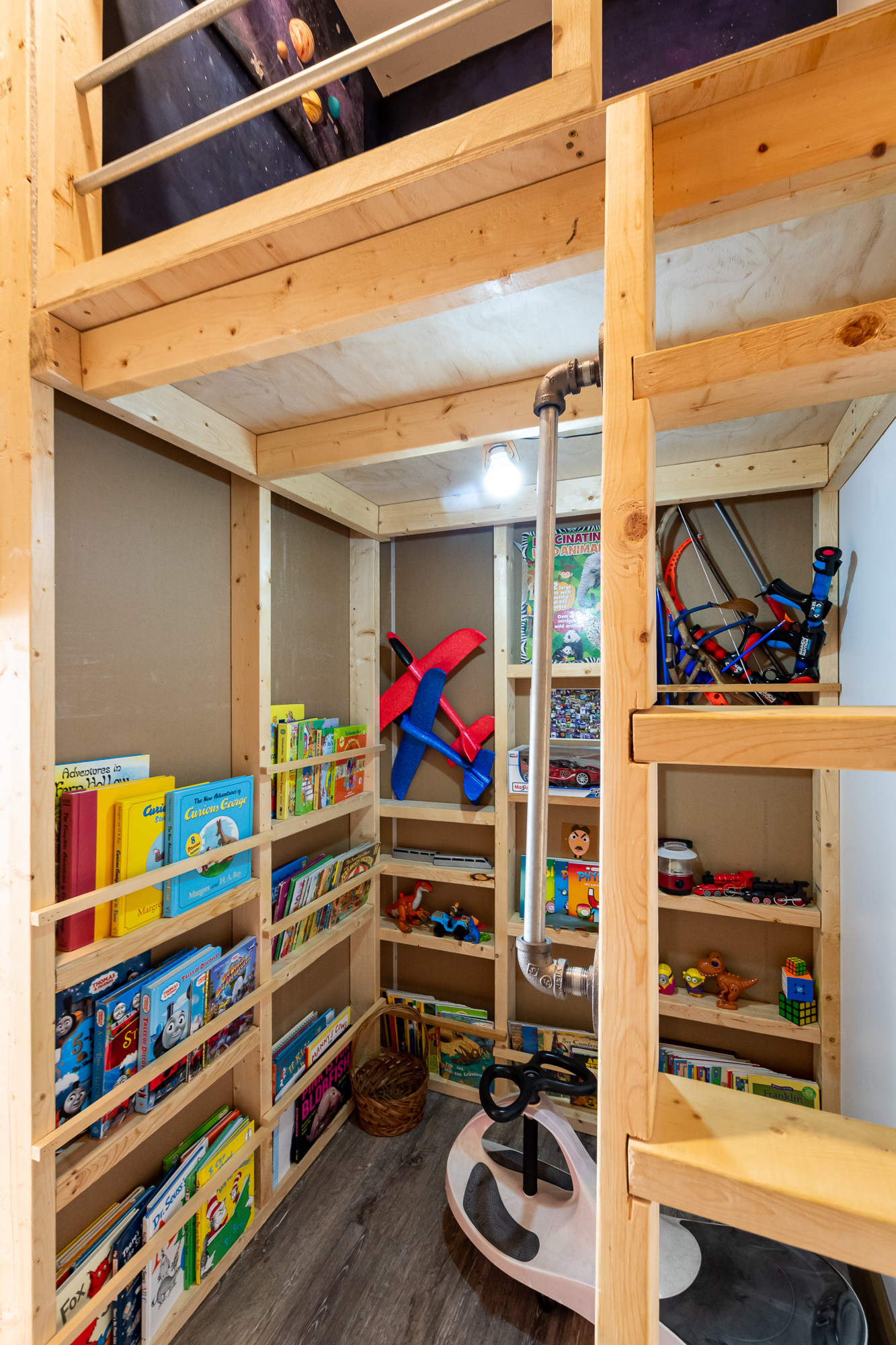 Underneath a wood loft bed is a play space with rustic bookshelves and toy storage