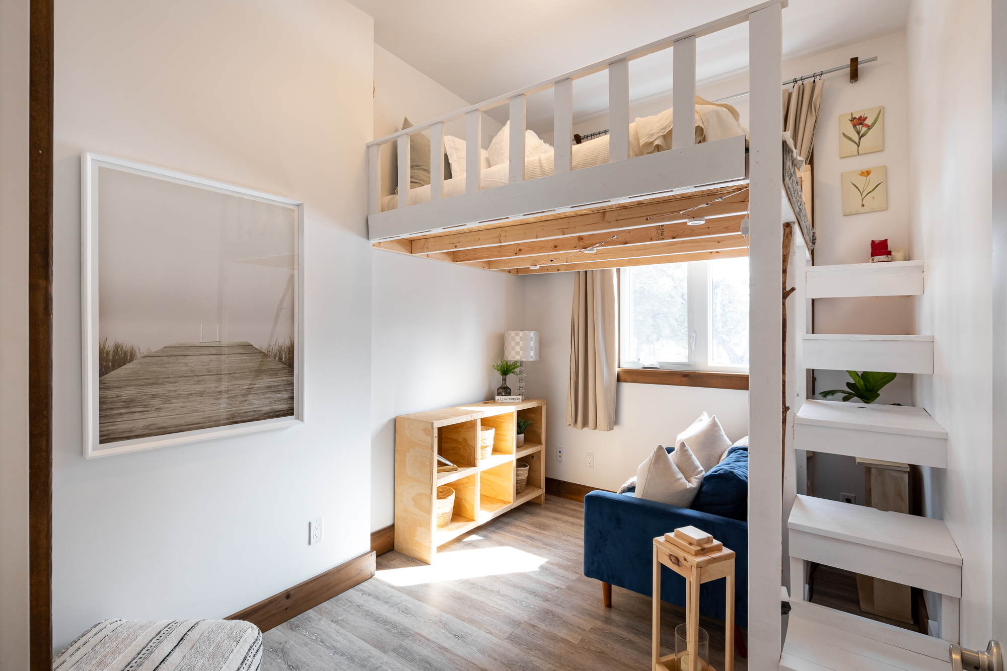 The first guest bedroom has a built-in loft bed with white stairs that lead to the bed. Underneath the loft is a blue couch