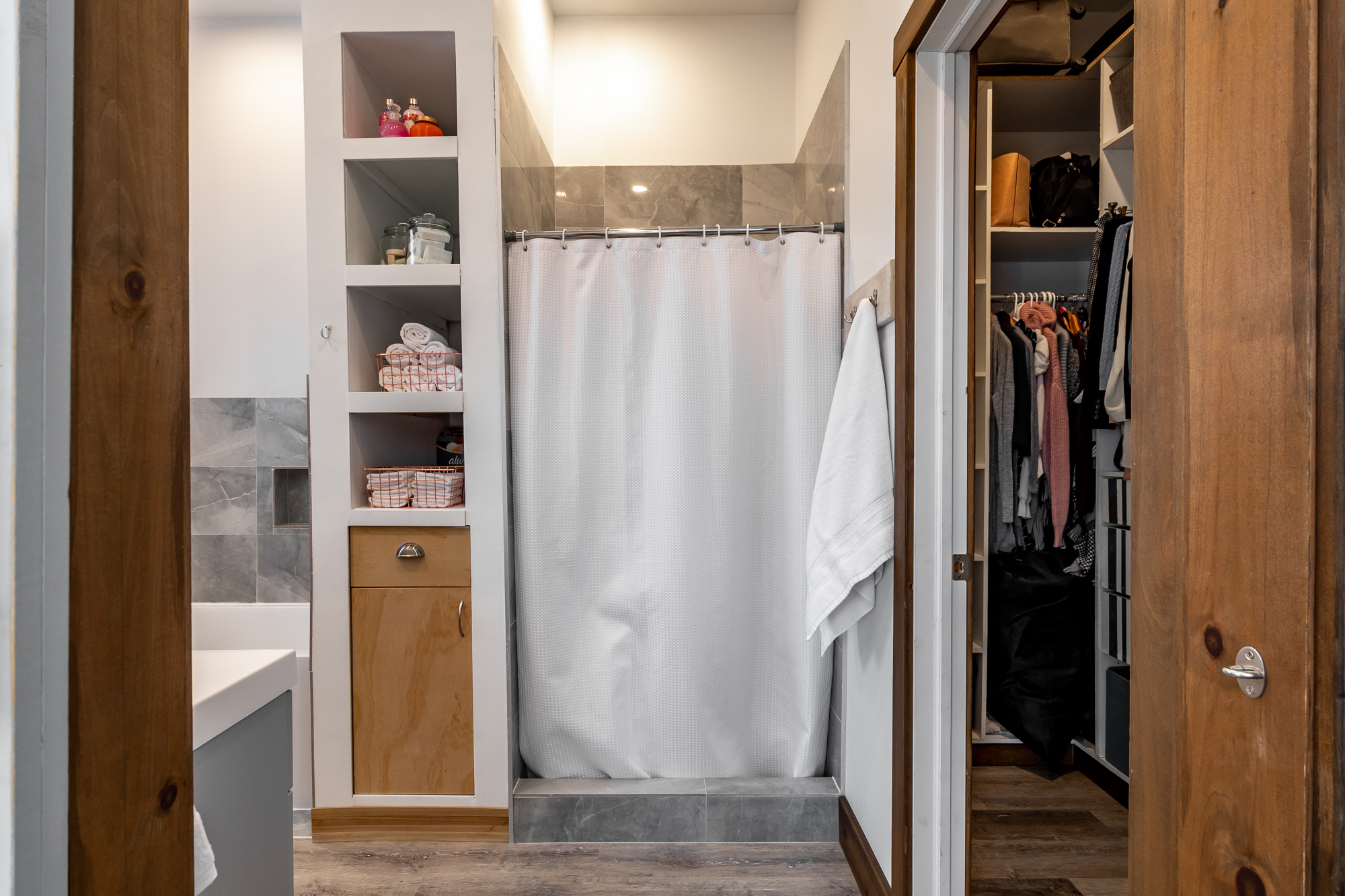 A shower covered by a white shower curtain. The rest of the bathroom is to the left, the walk-in closet is to the right