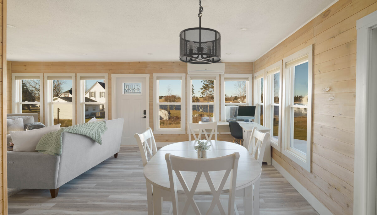 An open-concept dining and living space just inside a front door. Lots of windows let in natural light, and light wood panelling covers the walls.