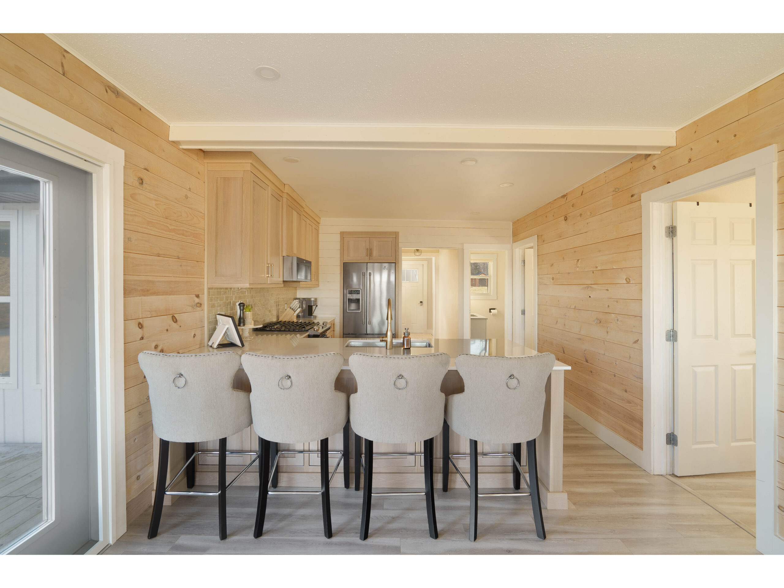 A small but open kitchen with a large peninsula and barstools, wooden cabinets that match the wood-panelled wall, and stainless steel appliances.